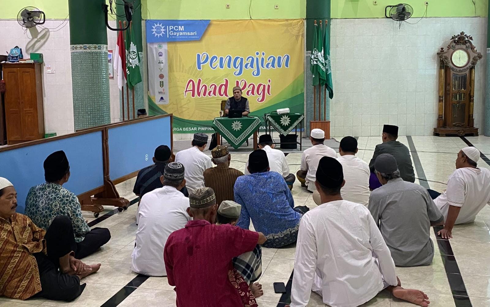 Suasana pengajian Ahad Pagi di dalam Masjid Taqwa Al Mukarromah Gayamsari yang memperlihatkan jamaah pria duduk bersila menyimak pemaparan Ust. Aang Kunaepi di depan spanduk besar berwarna kuning-hijau bertuliskan 'Pengajian Ahad Pagi'