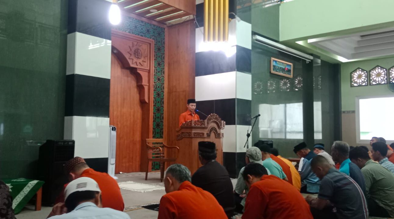 Suasana di dalam Masjid At Taqwa PDM Kota Semarang yang memiliki pilar hitam-putih. Terlihat Ustadz Sarmadi yang mengenakan kemeja berwarna jingga (orange) dan peci hitam berdiri di balik mimbar kayu berukir sedang memberikan ceramah kepada jamaah laki-laki yang duduk bersila menyimak dengan khidmat.