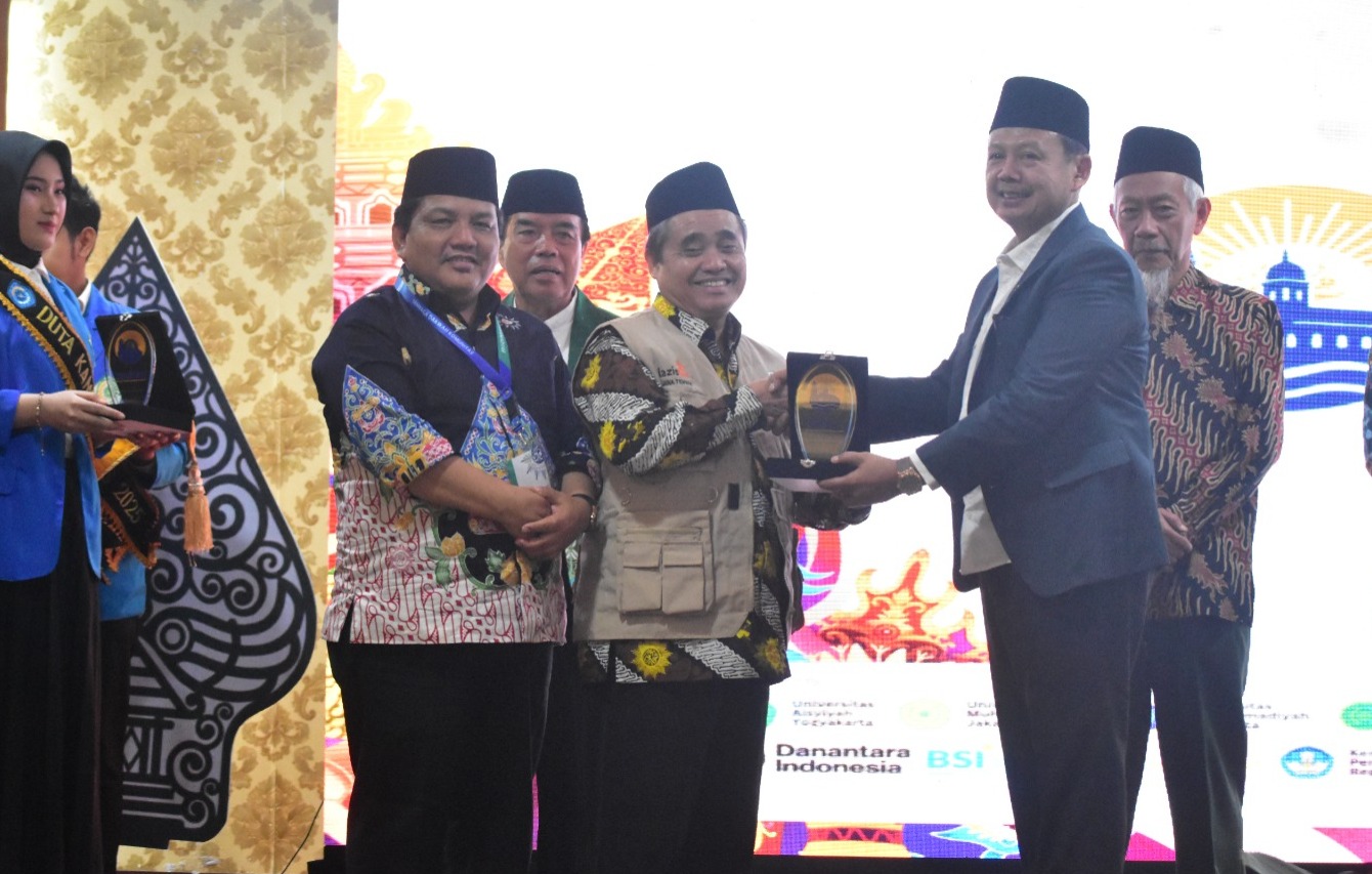 Suasana di atas panggung acara formal yang menampilkan Dr. KH. Tafsir, M.Ag. sedang berdiri di podium sebelah kiri sambil menunjuk ke arah layar digital besar. Layar tersebut menampilkan foto profil beliau yang sedang tersenyum dengan keterangan teks 'Dr. KH. Tafsir, M.Ag. Ketua PWM Jawa Tengah'. Di sisi panggung terdapat dekorasi wayang gunungan dan rangkaian bunga segar.
