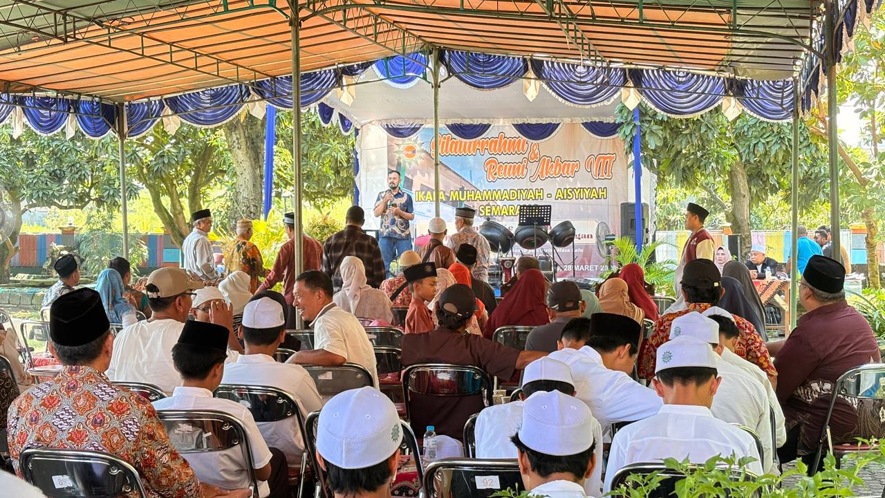 Foto suasana Reuni Akbar VII yang berlangsung di bawah tenda besar dengan dekorasi kain berwarna biru dan putih. Terlihat puluhan alumni duduk di barisan kursi lipat menghadap ke arah panggung. Di atas panggung, seorang pria mengenakan kemeja batik biru sedang berbicara menggunakan mikrofon di depan latar belakang banner acara bertuliskan "Silaturahmi & Reuni Akbar VII IKAPA-MUHAMMADIYAH-AISYIYAH SEMARANG". Jemaah pria yang duduk di barisan depan sebagian besar mengenakan peci hitam atau putih dan baju koko atau batik, menciptakan suasana kekeluargaan yang khidmat di area terbuka yang dikelilingi pepohonan.