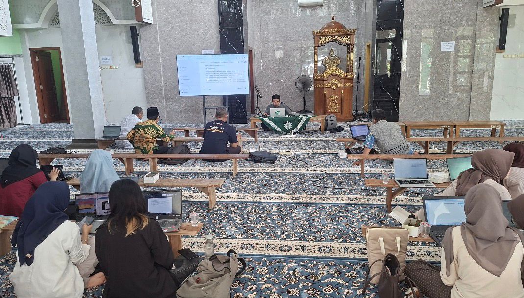 Suasana pelatihan AI pembuatan buku oleh PCM Gunungpati 2 di Masjid At-Taqwa. Tampak Dr. Kasmui (pakar AI UNNES) di depan layar monitor memberikan materi kepada dosen dan mahasiswa yang antusias menggunakan laptop di atas karpet.