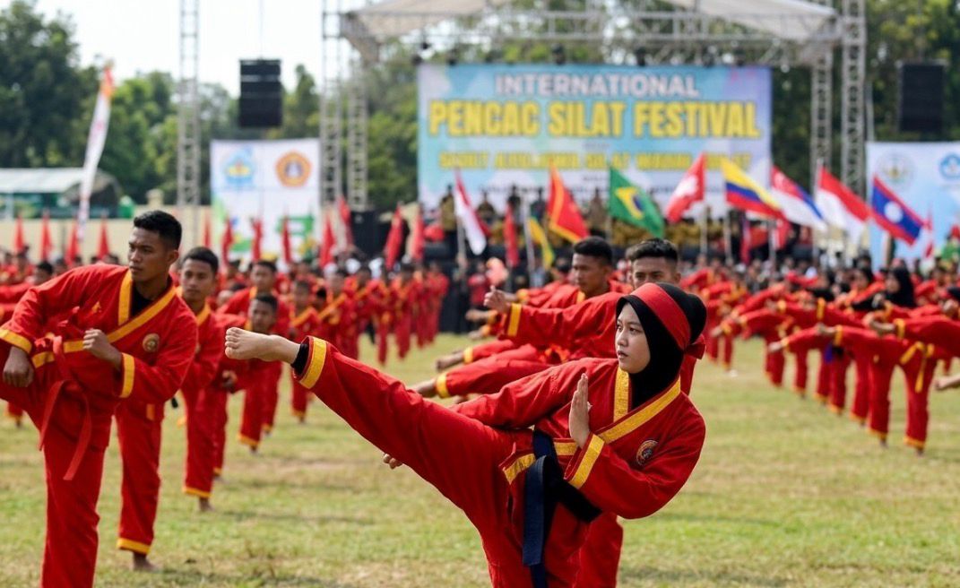 Pesilat Tapak Suci di Semarang sedang melakukan gerakan tendangan depan tinggi yang presisi sebagai bagian dari demonstrasi di depan panggung festival pencak silat internasional. Ratusan pesilat lainnya membentuk formasi latar belakang.