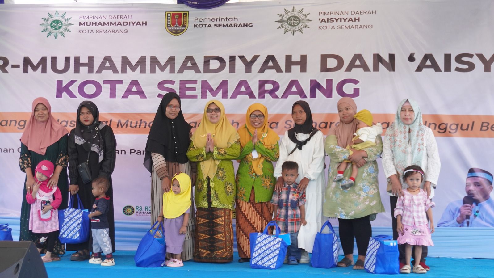Penyerahan simbolis paket nutrisi penanganan stunting oleh pimpinan 'Aisyiyah Kota Semarang kepada ibu dan balita di atas panggung acara Hari Bermuhammadiyah Genuk, latar belakang spanduk kolaborasi Pemerintah Kota Semarang dan Muhammadiyah.