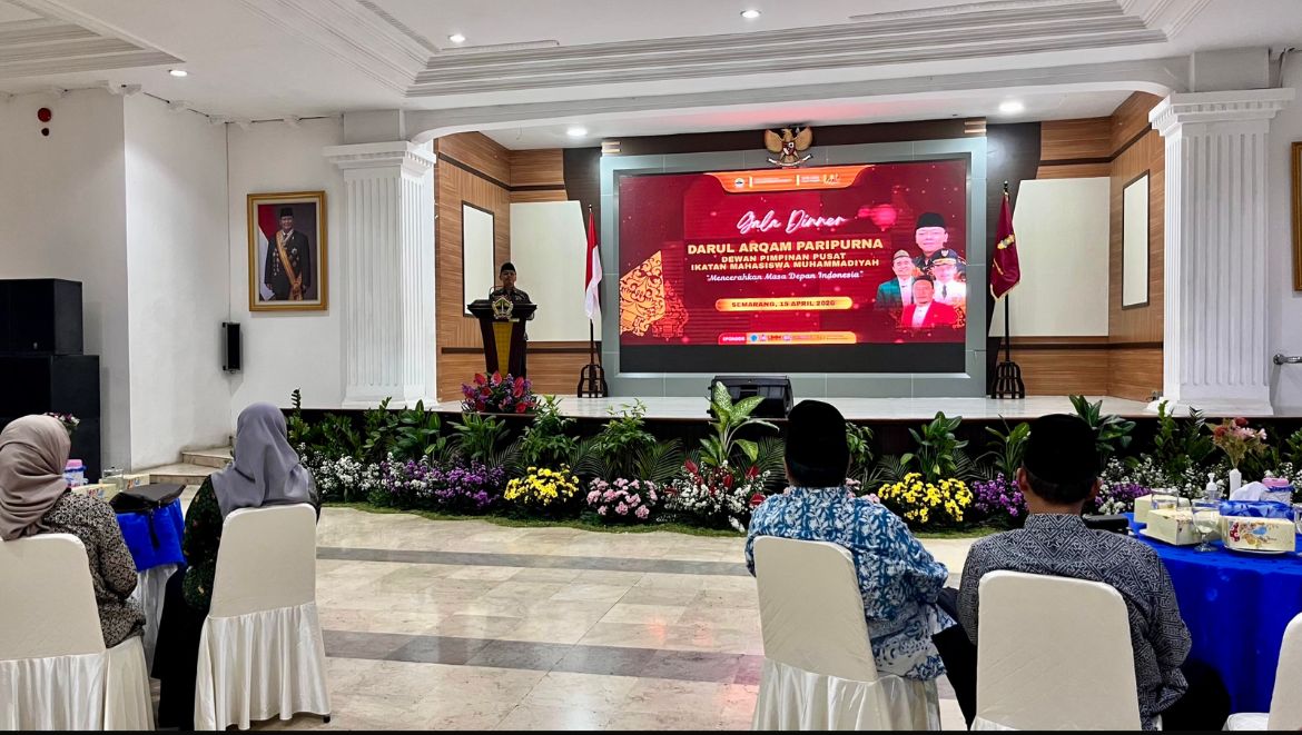 Foto suasana jamuan makan malam formal di dalam aula Wisma Perdamaian yang megah dengan pilar-pilar putih tinggi. Di latar depan, tampak deretan jamaah atau tamu undangan duduk rapi di kursi putih, membelakangi kamera. Di barisan depan panggung, terdapat rangkaian bunga hias berwarna-warni. Di atas panggung, seorang pria sedang berbicara di podium, didampingi oleh spanduk digital besar di layar LED bertuliskan "Gala Dinner DARUL ARQAM PARIPURNA DEWAN PIMPINAN PUSAT IKATAN MAHASISWA MUHAMMADIYAH 'Mencerahkan Masa Depan Indonesia' SEMARANG, 15 APRIL 2026". Suasana acara tampak hangat dan khidmat dengan pencahayaan ruangan yang terang.