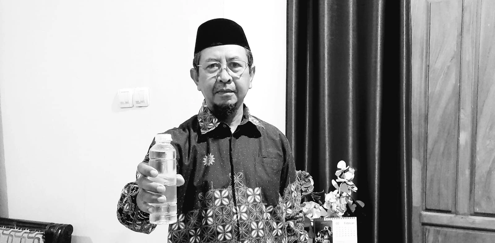 H. Mustain mengenakan peci dan kemeja batik memegang botol air kemasan, simbol inisiatif pabrik Air Minum Muhammadiyah di Semarang