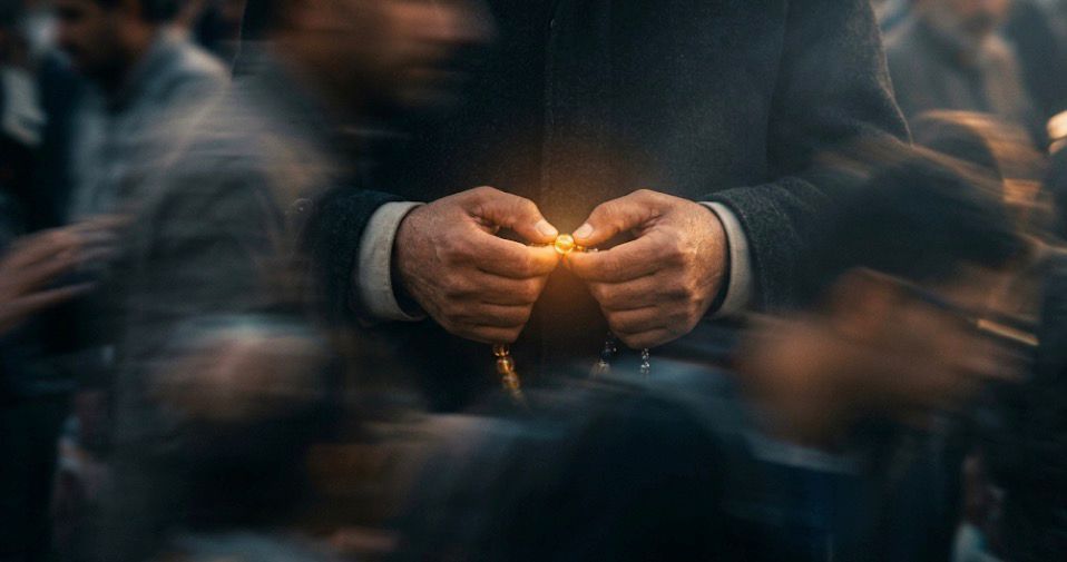 Seseorang memegang tasbih bercahaya di tengah kerumunan yang kabur sebagai simbol menjaga batasan ketaatan dalam Islam dan prinsip iman.