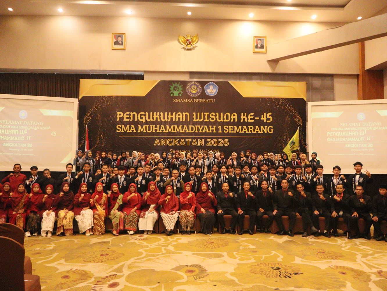 "Foto grup besar para wisudawan Angkatan 2026, guru, dan staf SMA Muhammadiyah 1 Semarang pada acara Pengukuhan Wisuda ke-45 di panggung aula dengan spanduk latar belakang besar bertuliskan 'SMAMSA BERSATU'."