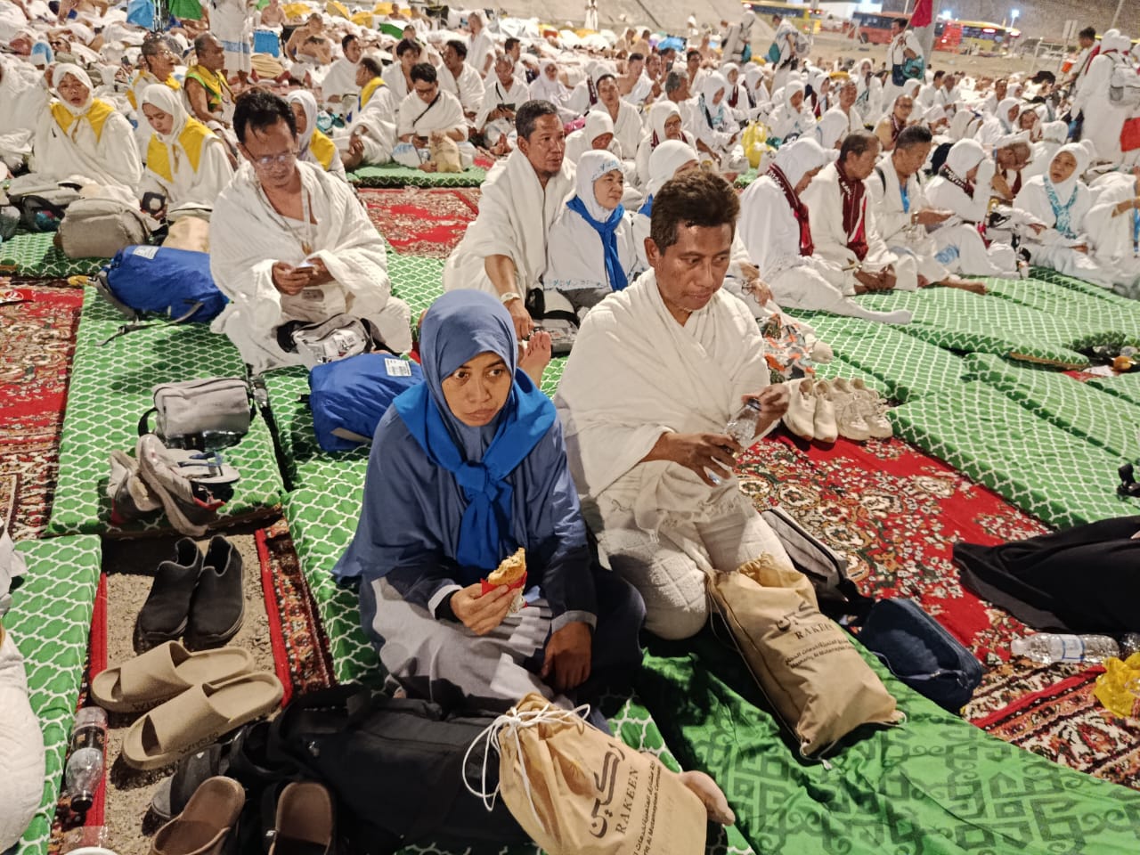 Suasana malam hari ratusan jemaah haji Indonesia saat mabit Muzdalifah, duduk dengan rapi di atas hamparan kasur busa empuk berwarna hijau dan karpet merah.