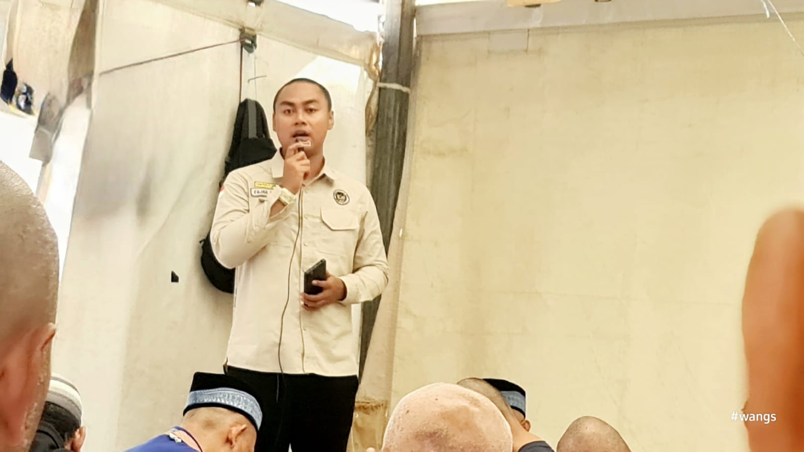 Petugas kesehatan Kloter 28 SOC Semarang sedang berdiri menyampaikan sosialisasi kesehatan darurat menggunakan mikrofon di hadapan para jemaah di dalam tenda Arafah yang tertib