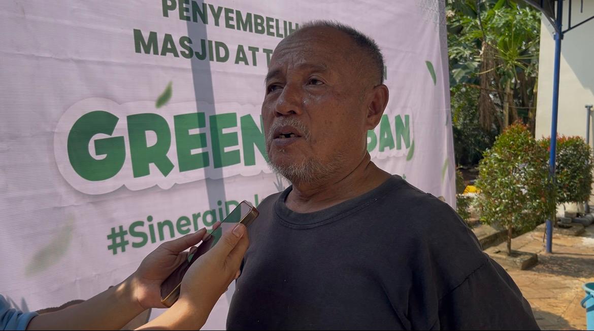 Pak Suharno, petani Semarang berbaju hitam, sedang diwawancarai menggunakan ponsel saat menceritakan kisah keikhlasan ibadah kurban di Masjid At-Taqwa Ngaliyan.