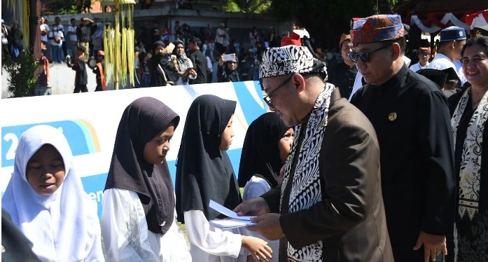Mendikdasmen Abdul Mu'ti memberikan dokumen bantuan kepada seorang siswi berpakaian putih dan berkerudung dalam upacara Hardiknas 2026 di Banyuwangi.