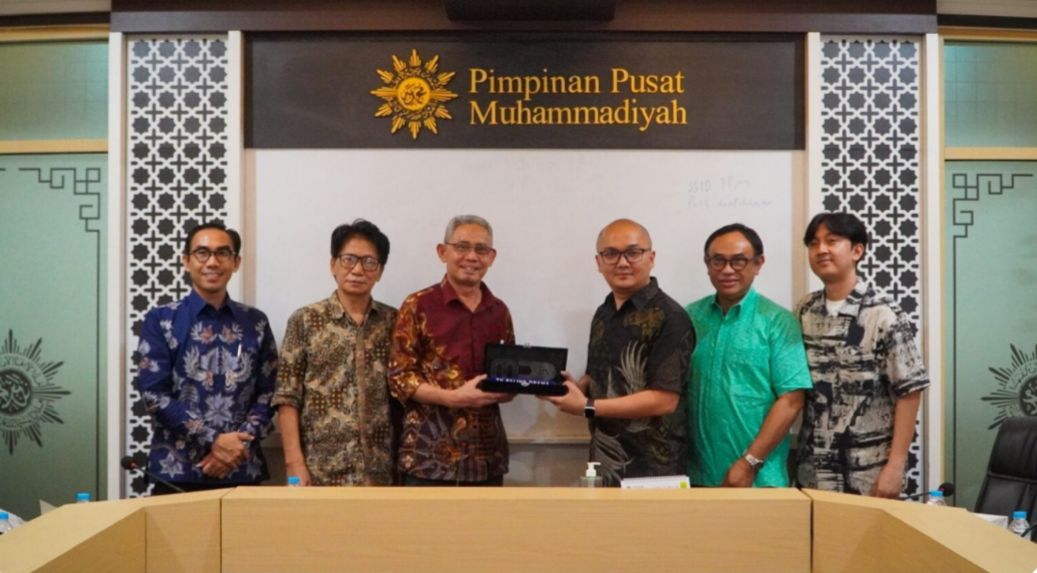 Foto dokumentasi pertemuan resmi di kantor Pimpinan Pusat (PP) Muhammadiyah. Tampak jajaran pimpinan Muhammadiyah, termasuk Irwan Akib dan Gunawan Budiyanto, berfoto bersama jajaran direksi MD Pictures. Di tengah barisan, terlihat produser Manoj Punjabi yang mengenakan kemeja biru muda. Anggota delegasi Muhammadiyah mengenakan kemeja batik dan peci hitam. Mereka berdiri berjajar di depan latar belakang dinding kayu dengan logo resmi Muhammadiyah yang besar di bagian tengah, menciptakan suasana formal namun hangat.