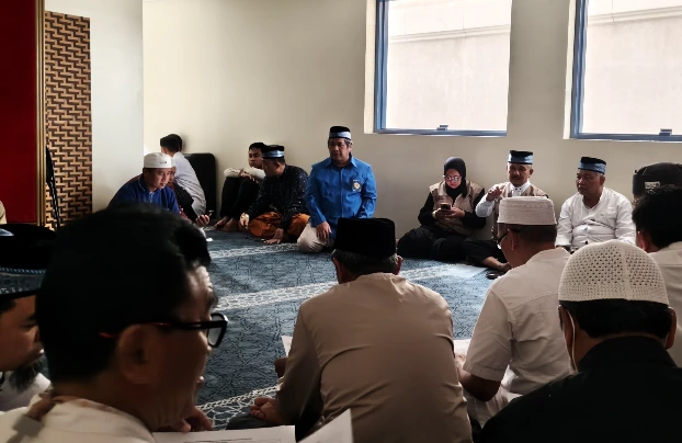 Sekelompok jemaah haji pria duduk melingkar lesahan di atas karpet bersama petugas haji yang mengenakan batik TPIHI dan pembimbing KBIHU, tampak sedang berdiskusi santai dan ramah tamah di musala hotel.