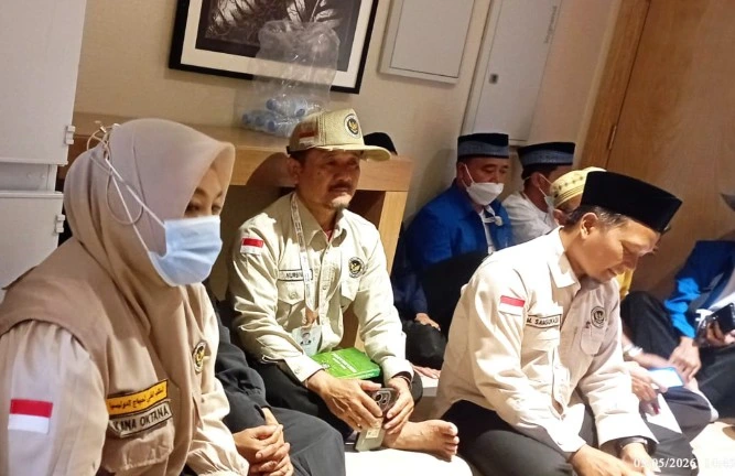 Ustadz Nurbini bertopi bersama petugas PPIH dan perangkat Kloter 28 SOC Semarang sedang duduk lesehan melangsungkan rapat koordinasi membahas tindak lanjut larangan city tour haji 2026 di Madinah.