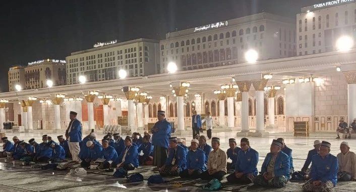 Puluhan jemaah haji laki-laki Kloter 28 SOC Semarang berseragam biru duduk bersila melaksanakan salat tahajud di rooftop Masjid Nabawi pada dini hari dengan latar belakang pilar dan lampu pelataran masjid.
