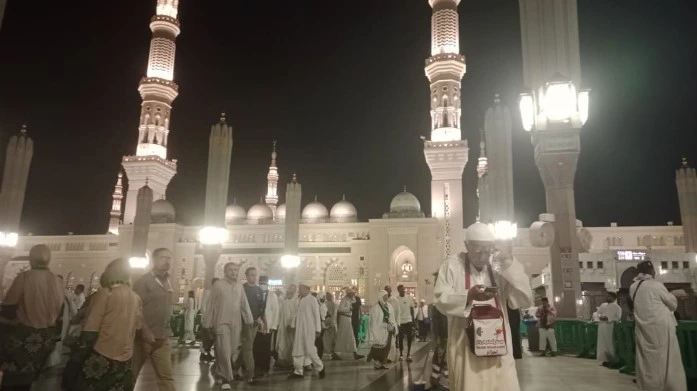 Ribuan jemaah melangkah tenang di pelataran Masjid Nabawi Haji 2026 pada malam hari dengan latar menara bercahaya keemasan.