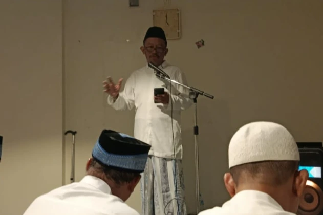 Jemaah Haji Indonesia kloter 28 SOC duduk bersila di karpet hijau musala penginapan membaca Al-Qur'an dan berzikir.