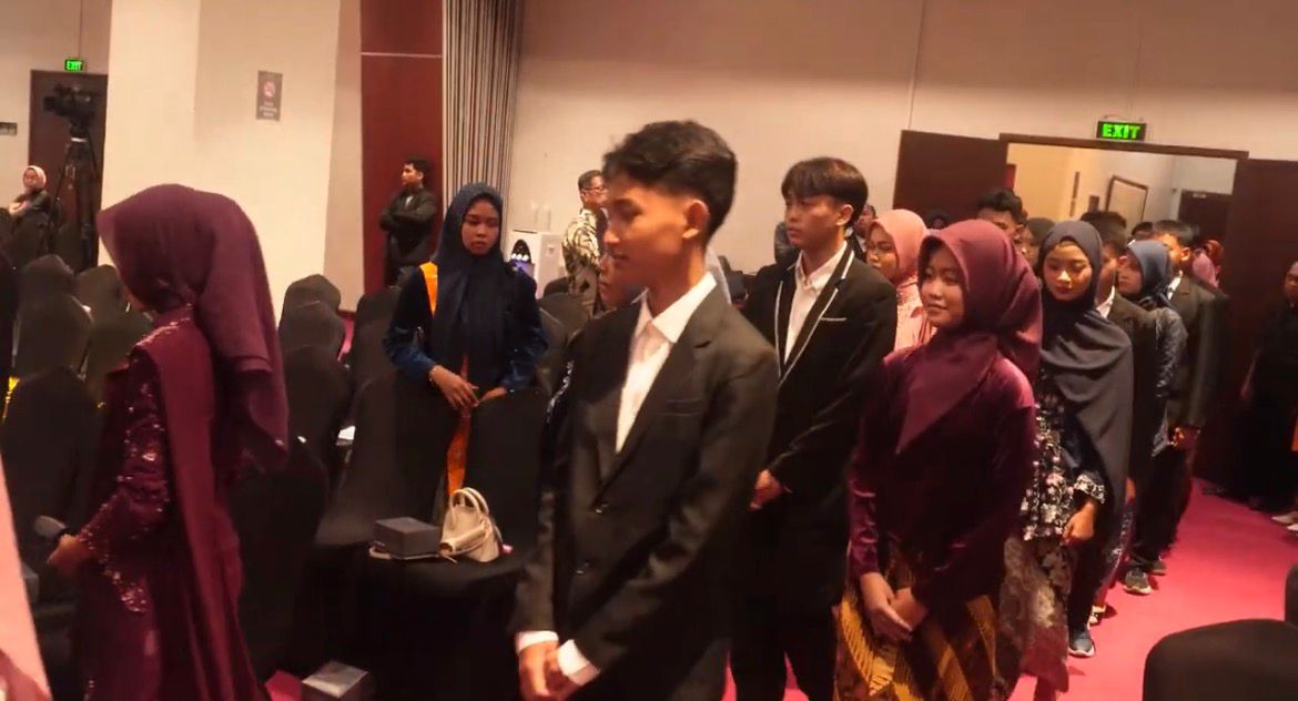 Barisan siswa laki-laki dan perempuan SMP Muhammadiyah 3 Semarang yang mengenakan jas hitam formal dan kebaya brokat berwarna ungu berjalan beriringan dengan tertib dan khidmat di dalam ruang pertemuan hotel.