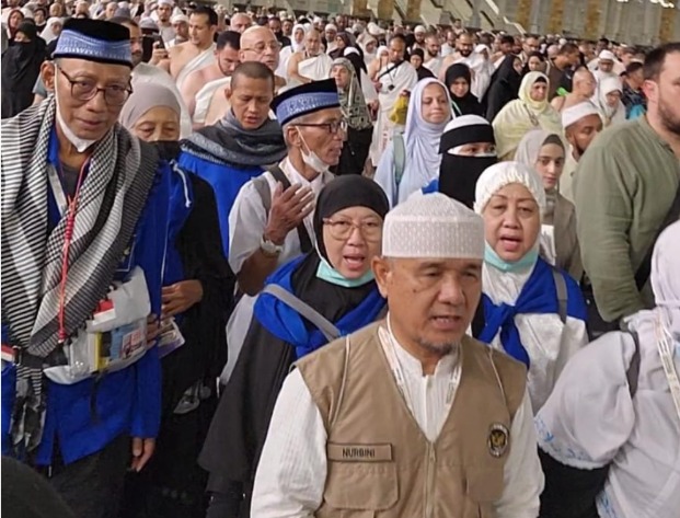 Tim Pembimbing Ibadah Haji Indonesia, Nurbini, mengenakan rompi cokelat memimpin rombongan jemaah haji Kloter 28 SOC yang memakai seragam batik haji biru di tengah kepadatan Masjidil Haram saat bersiap tawaf wada.