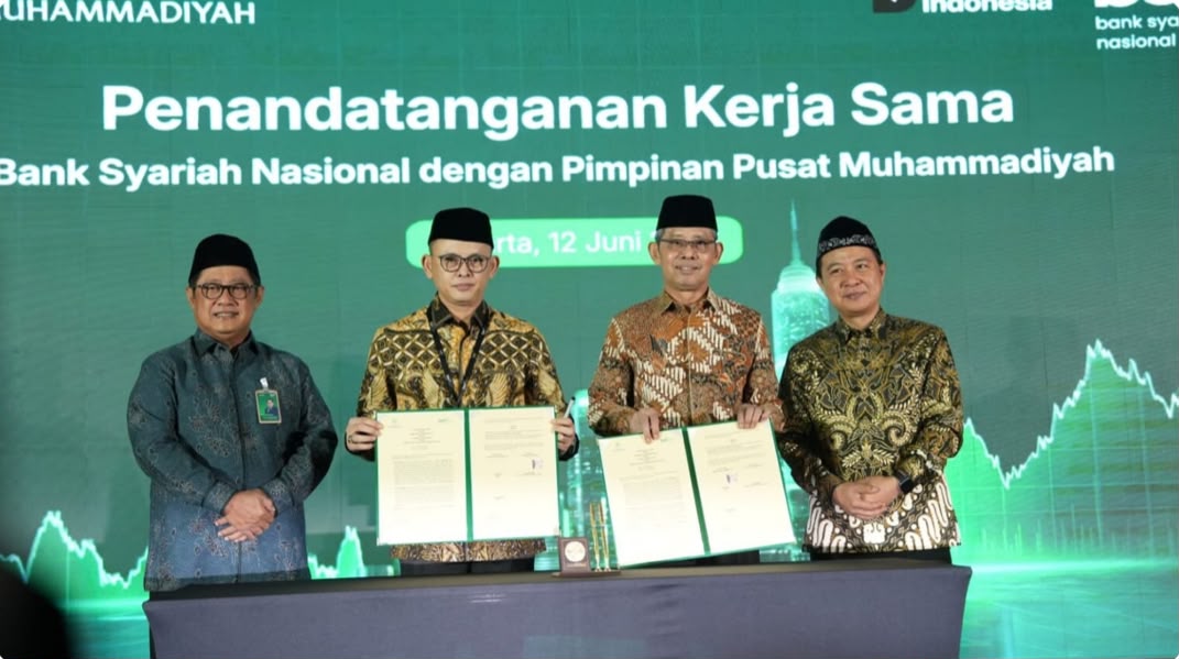 Foto dokumentasi empat tokoh pimpinan berpeci hitam dan berkemeja batik berdiri berjejer di atas panggung dalam sebuah acara resmi. Dua tokoh di tengah tersenyum lebar sambil memegang map hijau terbuka berisi dokumen Perjanjian Kerja Sama (PKS) yang telah ditandatangani. Di latar belakang tampak layar hijau besar dengan tulisan putih "Penandatanganan Kerja Sama Bank Syariah Nasional dengan Pimpinan Pusat Muhammadiyah, Jakarta, 12 Juni 2026".