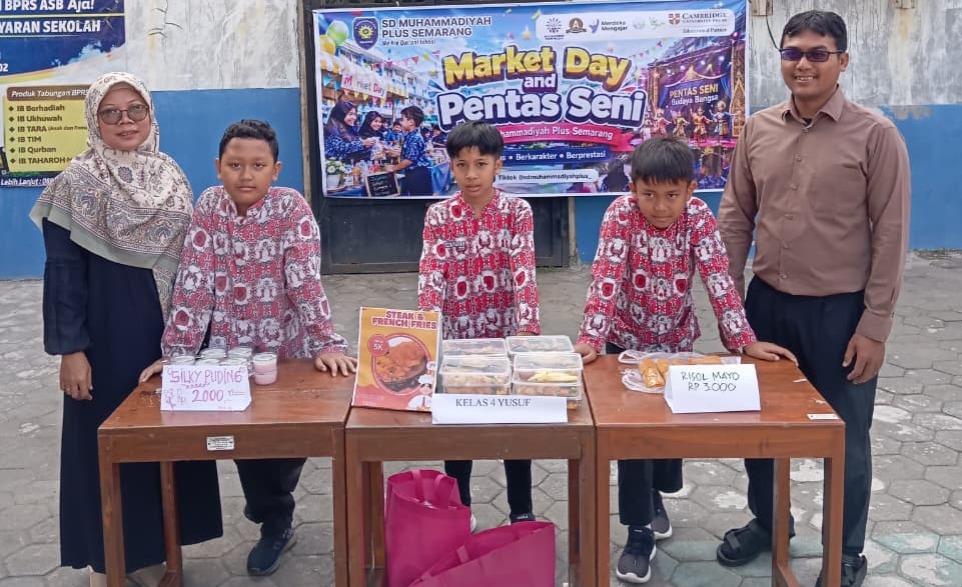 Foto dokumentasi tiga siswa sekolah dasar laki-laki mengenakan seragam batik merah khas Muhammadiyah berdiri dengan bangga di belakang stan meja kayu jajanan mereka. Mereka didampingi oleh seorang guru perempuan berhijab biru tua di sisi kiri dan seorang guru laki-laki berkemeja cokelat di sisi kanan. Di atas meja tersaji produk kuliner seperti silky puding, steak & french fries, serta risol mayo dengan label harga tertulis rapi. Latar belakang menampilkan spanduk besar acara "Market Day and Pentas Seni SD Muhammadiyah Plus Semarang".