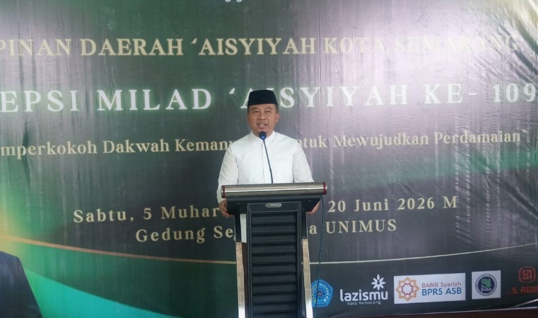 Foto dokumentasi Dr. Elly Asmara, S.STP., M.M. (Kepala Bagian Kesejahteraan Rakyat Setda Kota Semarang) yang mengenakan peci hitam dan kemeja putih sedang berbicara dengan tenang di balik podium hitam dalam acara Resepsi Milad ke-$109$ Pimpinan Daerah Aisyiyah Kota Semarang. Di latar belakang, tampak spanduk hijau besar bertuliskan "Pimpinan Daerah 'Aisyiyah Kota Semarang Resepsi Milad 'Aisyiyah ke-109" serta logo Lazismu, BPRS ASB, dan mitra lainnya di bagian bawah. Foto dokumentasi ini tersimpan dalam berkas WhatsApp Image 2026-06-20 at 19.47.09.jpeg yang menggambarkan apresiasi pemerintah terhadap kiprah gerakan perempuan aisyiyah dalam pembangunan kesejahteraan sosial.