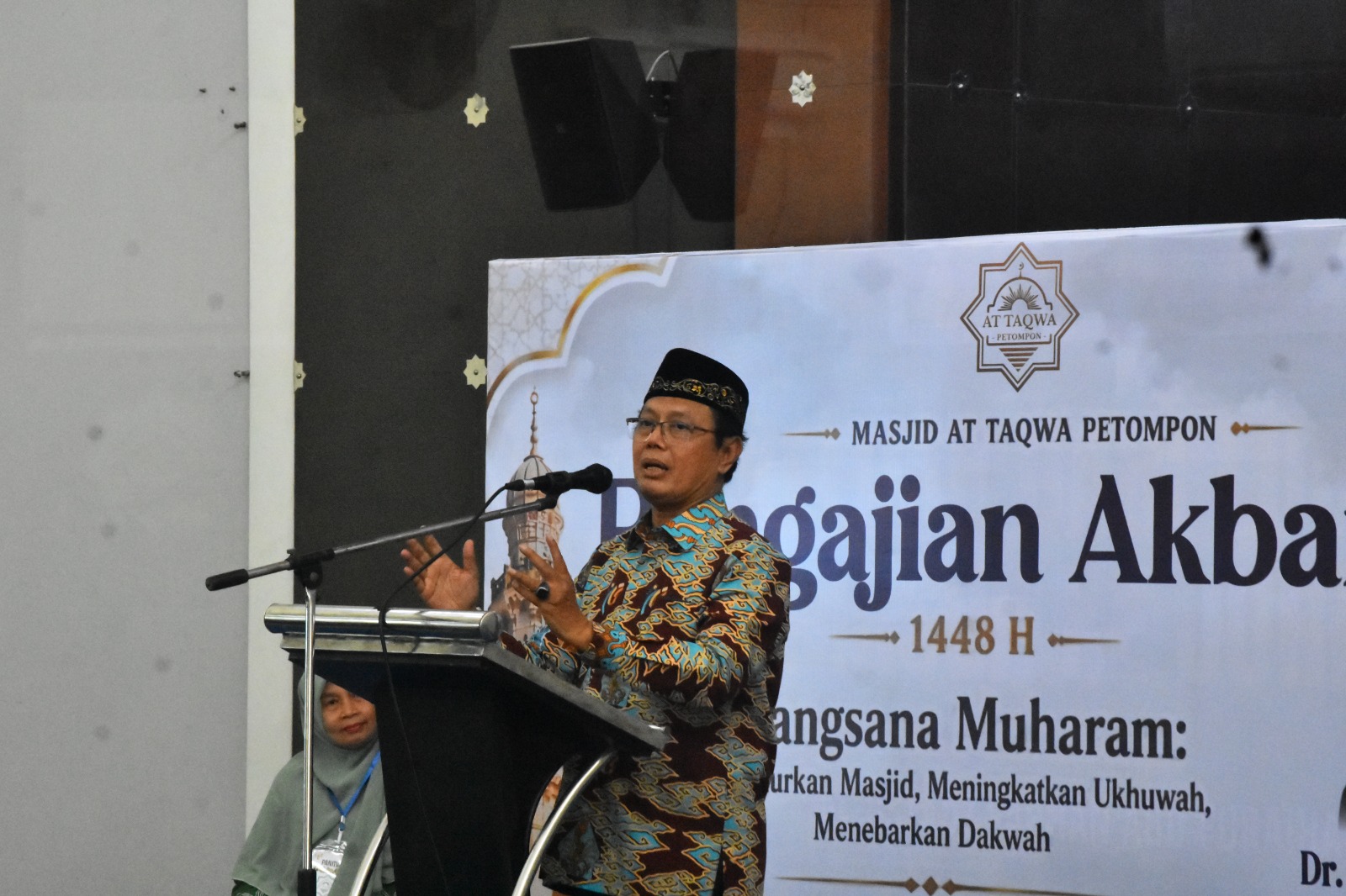 Foto dokumentasi Ketua PDM Kota Semarang Dr. KH. Fachrur Rozi, M.Ag. mengenakan peci hitam dan kemeja batik bermotif awan biru-emas sedang berbicara secara ekspresif di balik podium. Di sebelah kanan beliau tampak latar belakang baliho putih bertuliskan "Masjid At Taqwa Petompon - Pengajian Akbar 1448 H