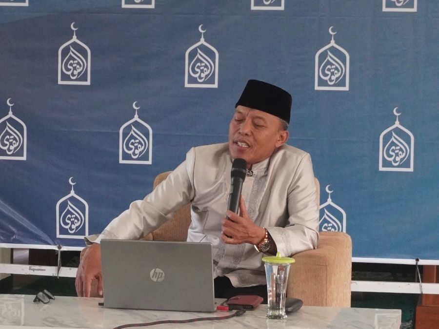 Foto Ustadz Djajuli sedang memberikan ceramah di depan jamaah Pengajian Ahad Pagi Semarang dengan latar belakang spanduk biru bermotif kubah masjid.