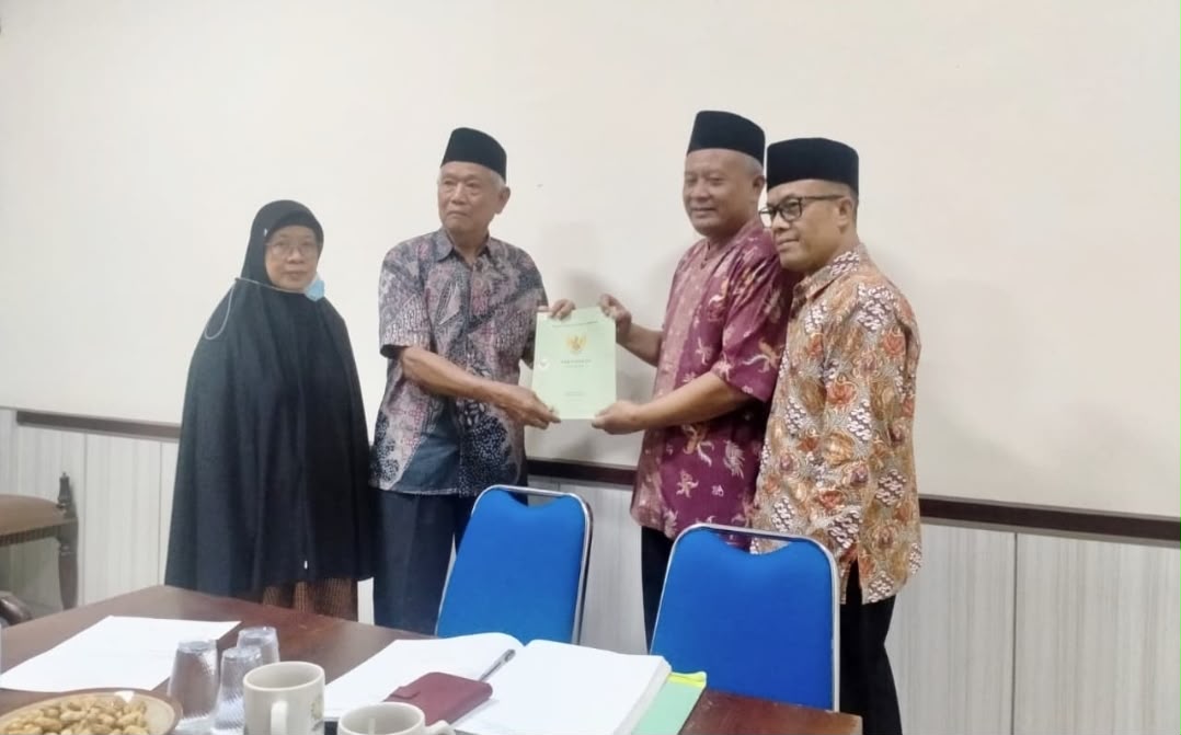 Foto bersama empat orang di dalam ruang rapat PDM Kota Semarang. Di sebelah kiri berdiri seorang wanita berhijab hitam dan pria lansia berkemeja batik abu-abu yang sedang menyerahkan map dokumen resmi berwarna hijau muda kepada pria berkemeja batik merah marun di sebelahnya. Di sebelah kanan, berdiri pria berkacamata dengan kemeja batik emas kecokelatan menyaksikan prosesi tersebut dengan senyum ramah. Di latar depan tampak meja rapat kayu dengan beberapa kertas dokumen, cangkir putih, dan piring camilan.