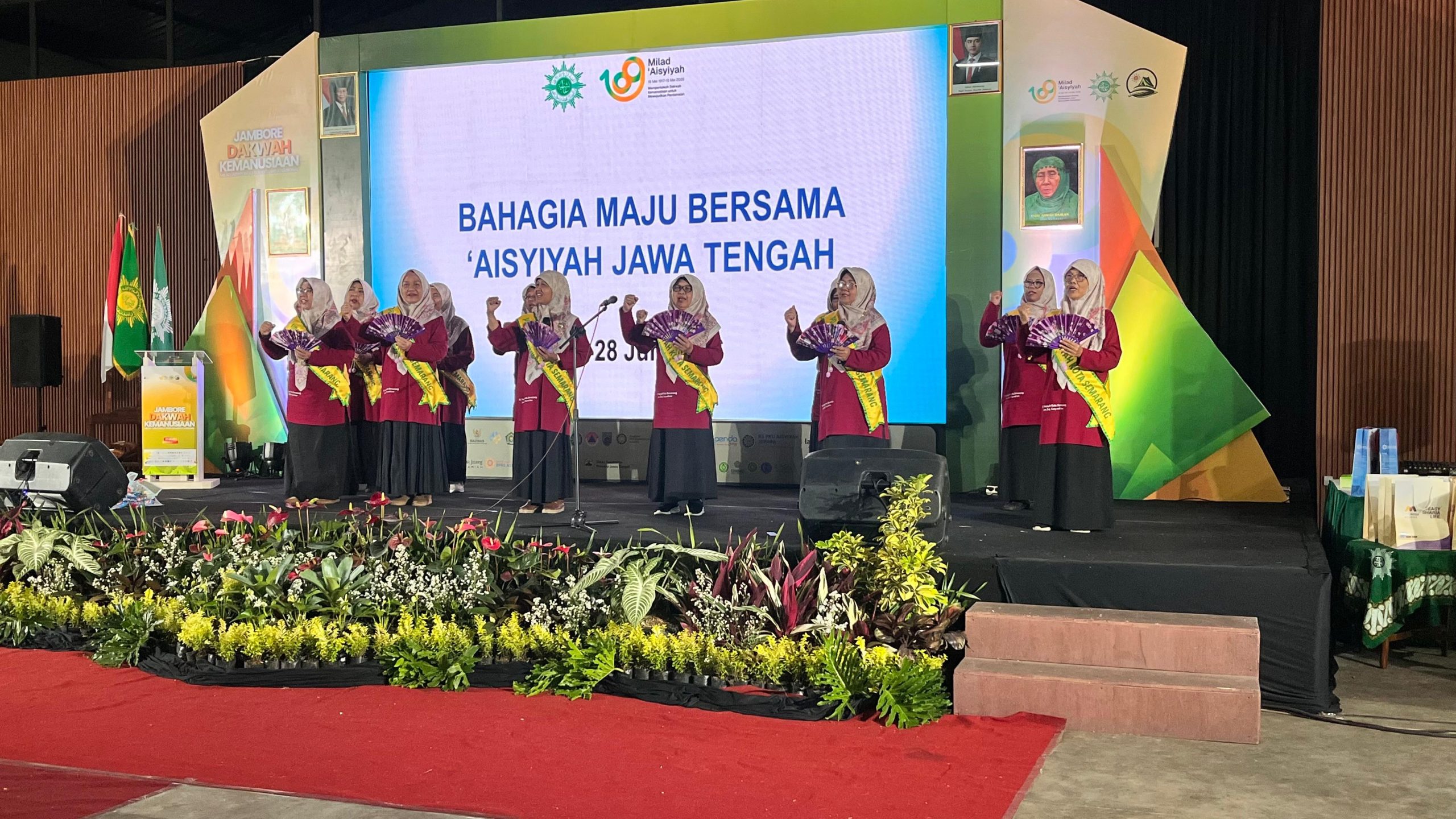 Foto bersama sepuluh perempuan anggota PDA Kota Semarang berhijab abu-abu dan berseragam marun dengan selempang kuning bertuliskan PDA KOTA SEMARANG sedang tampil menyanyi di atas panggung. Beberapa di antaranya membawa kipas ungu dan sebagian lainnya mengepalkan tangan dengan semangat. Di latar belakang tampak layar LED besar bertuliskan BAHAGIA MAJU BERSAMA AISYIYAH JAWA TENGAH di bawah sorotan lampu panggung yang terang.