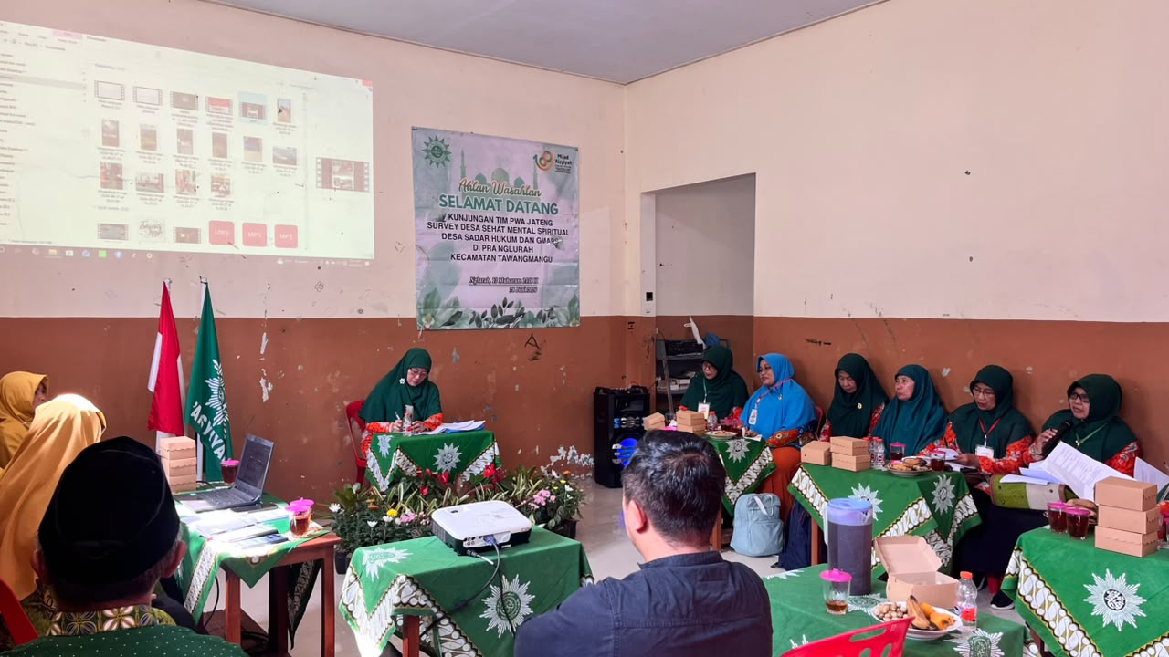 Foto suasana pertemuan resmi antara Tim PWA Jawa Tengah, PDA Kota Semarang, dan PRA Nglurah di dalam sebuah ruangan kelas. Tampak spanduk hijau bertuliskan "Kunjungan Tim PWA Jateng Survey Desa Sehat Mental Spiritual di PRA Nglurah" terpasang di dinding tengah. Sejumlah pengurus perempuan berpakaian hijau khas 'Aisyiyah duduk tertib menyimak di meja-meja berbalut taplak batik matahari Muhammadiyah, lengkap dengan kotak hidangan serta sorotan proyektor menyala di sisi kiri.