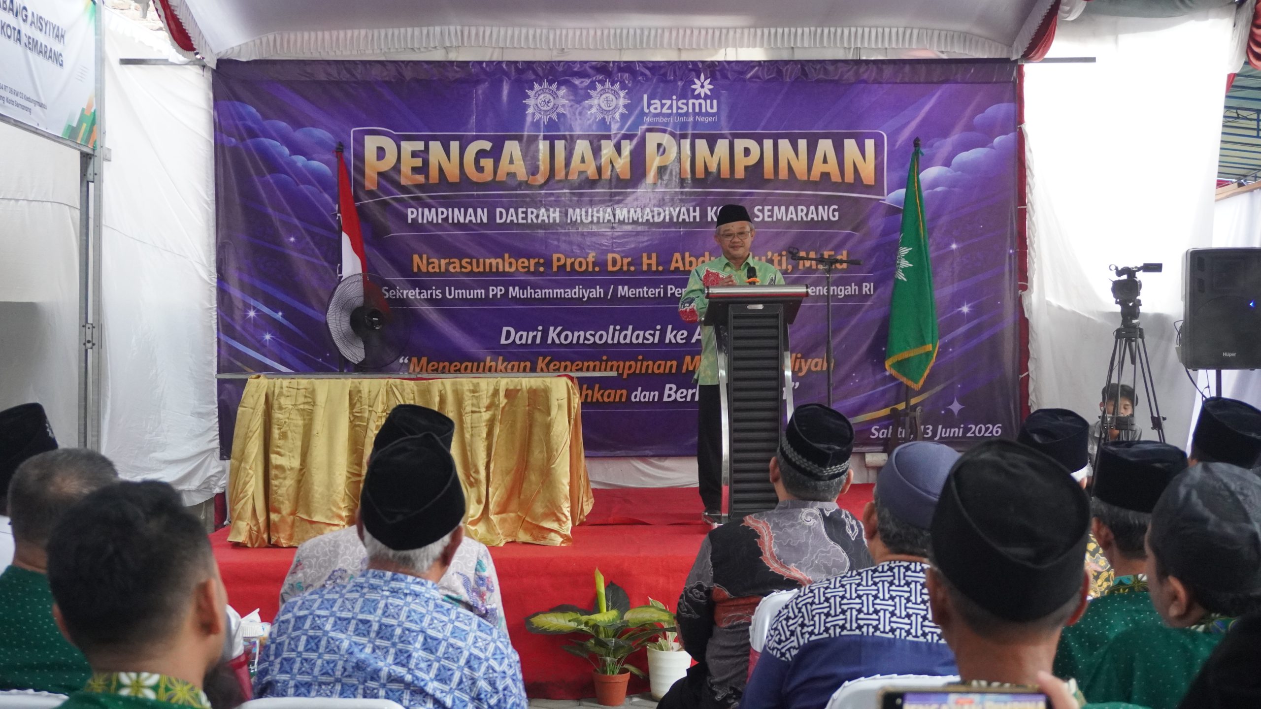 Foto dokumentasi suasana pengajian di dalam ruangan yang cukup luas. Tampak Prof. Dr. H. Abdul Mu'ti, M.Ed. sedang berdiri berwibawa di balik podium besi di atas panggung utama, mengenakan kemeja batik hijau bermotif dan peci hitam. Panggung tersebut berlatarkan spanduk ungu besar bertuliskan "Pengajian Pimpinan Pimpinan Daerah Muhammadiyah Kota Semarang" lengkap dengan logo Lazismu di bagian atas. Di latar depan bawah, barisan jemaah pria berkopiah hitam tampak duduk tertib membelakangi kamera menyimak materi ceramah
