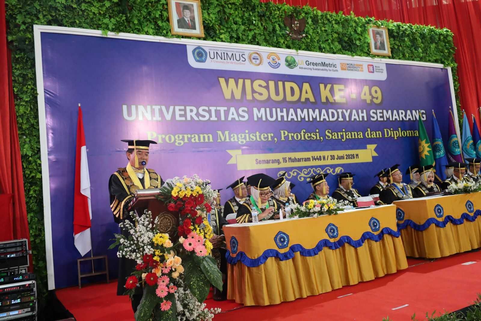 Rektor Universitas Muhammadiyah Semarang, Prof. Dr. Masrukhi, M.Pd., memberikan sambutan dari podium berhias bunga pada Sidang Terbuka Wisuda Ke-49 Universitas Muhammadiyah Semarang, 30 Juni 2026, di hadapan jajaran senat dan di depan backdrop acara.