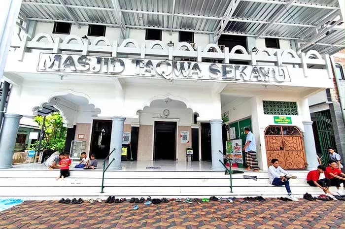 Bangunan depan Masjid At-Taqwa Sekayu Semarang dengan warga dan anak-anak duduk santai di pelataran, melambangkan kerukunan umat dan persatuan NU dan Muhammadiyah.