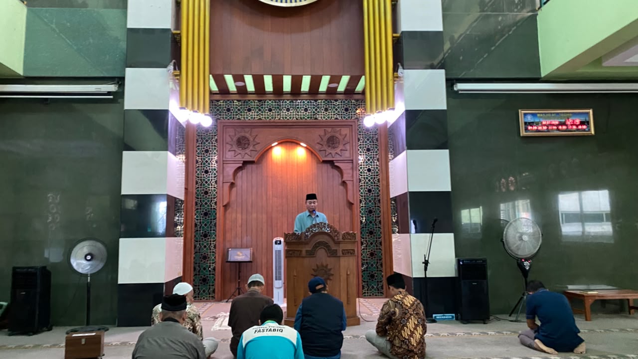 Ustadz Mukri berdiri di atas mimbar kayu Masjid At Taqwa PDM Kota Semarang saat menyampaikan materi Tafsir Surah Quraisy tentang rahasia ketenangan jiwa. Di depan mimbar, tampak beberapa jamaah pria sedang duduk mendengarkan khotbah dengan latar belakang dinding masjid bernuansa hijau tua dan pilar hitam-putih.