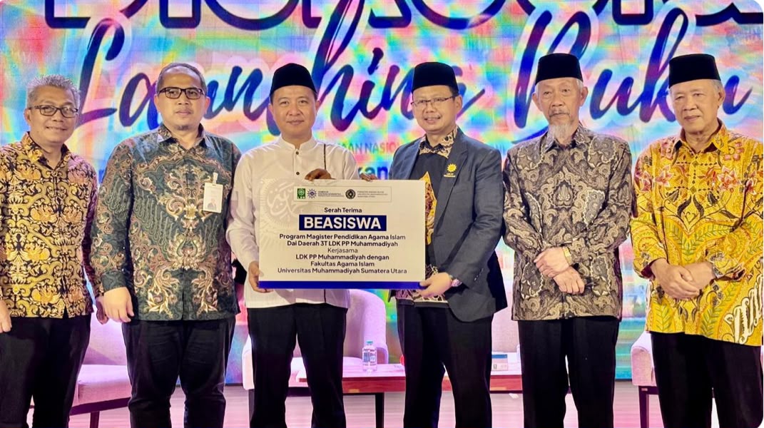 Prosesi penyerahan simbolis papan beasiswa dai muhammadiyah untuk Program Magister Pendidikan Agama Islam. Tampak Hilman Latief, Muchamad Arifin, Kiai Saad Ibrahim, Syamsul Anwar, dan jajaran pimpinan lainnya berdiri bersama di atas panggung dengan latar belakang layar digital bertuliskan "Launching Buku".