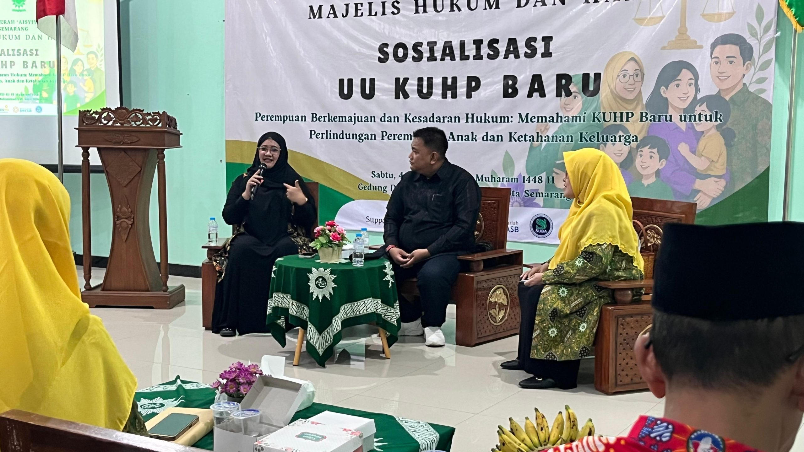 Tiga narasumber duduk di panggung dalam acara Sosialisasi UU KUHP Baru di Gedung PDM Kota Semarang untuk membedah perluasan Jerat Hukum Pelecehan Verbal. Pembicara wanita berhijab hitam tampak berbicara dengan mikrofon, didampingi pembicara pria berbaju hitam dan pembicara wanita berhijab kuning di depan spanduk acara.