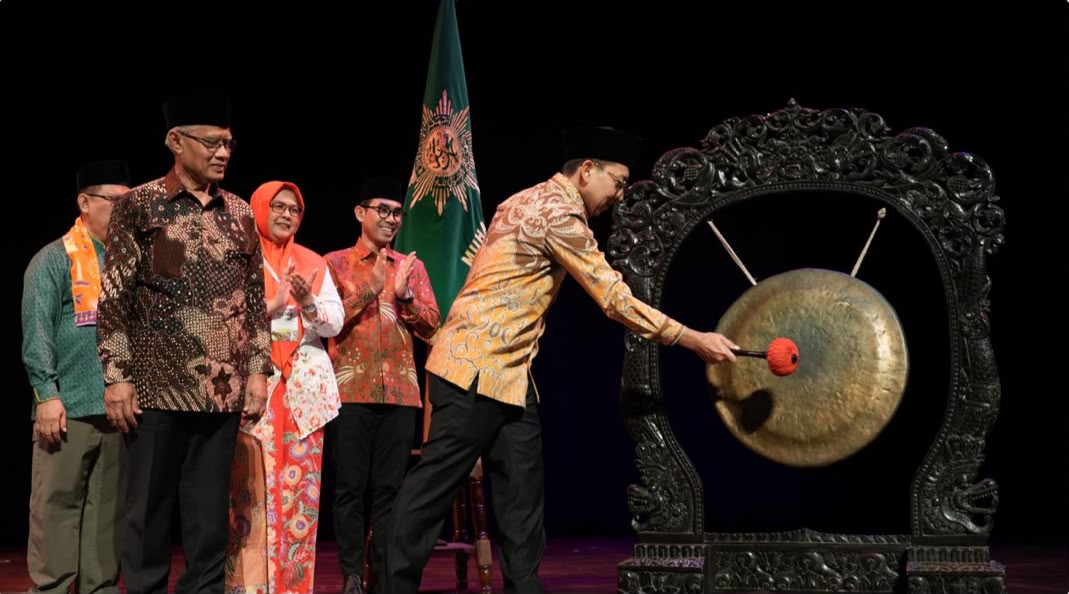 Menteri Kebudayaan Fadli Zon mengenakan batik cokelat-kuning dan peci hitam sedang memukul gong besar sebagai simbol pembukaan Rakernas Lembaga Seni Budaya PP Muhammadiyah untuk menjaga eksistensi seni budaya nusantara. Di sebelah kirinya, jajaran pimpinan organisasi termasuk Haedar Nashir menyaksikan prosesi dengan bertepuk tangan di atas panggung.