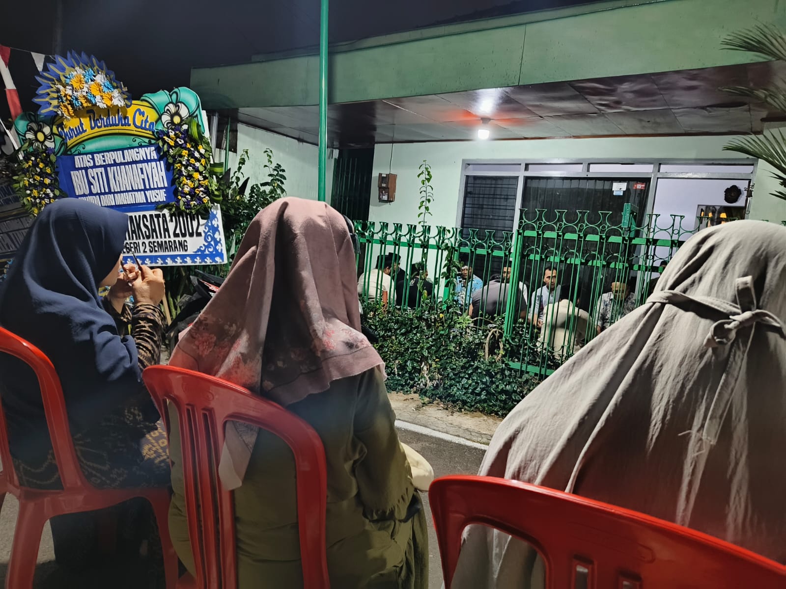 Para pelayat dan kader perempuan 'Aisyiyah yang mengenakan jilbab duduk berderet di depan rumah duka Ibu Siti Khanafiyah, seorang tokoh aisyiyah semarang, diiringi karangan bunga duka cita pada malam hari.