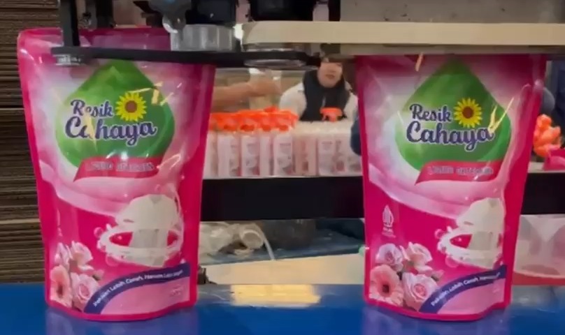 Kemasan pouch sabun pembersih kebutuhan rumah tangga merek "Resik Cahaya" berwarna merah muda dalam proses produksi dan pengemasan, mengilustrasikan gerakan ekonomi kreatif berbasis masjid untuk kemandirian umat.