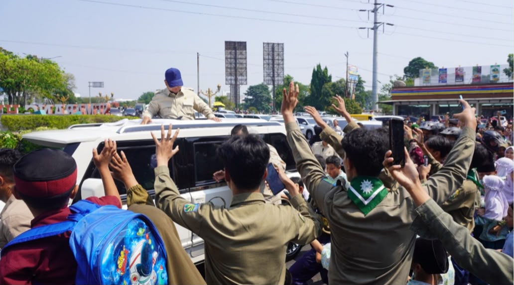 Presiden Prabowo Subianto berdiri di atas atap terbuka (sunroof) mobil SUV putih menyapa dan membagikan kenang-kenangan kepada siswa SMK Muhammadiyah 1 Semarang yang antusias menyambut di tepi jalan.