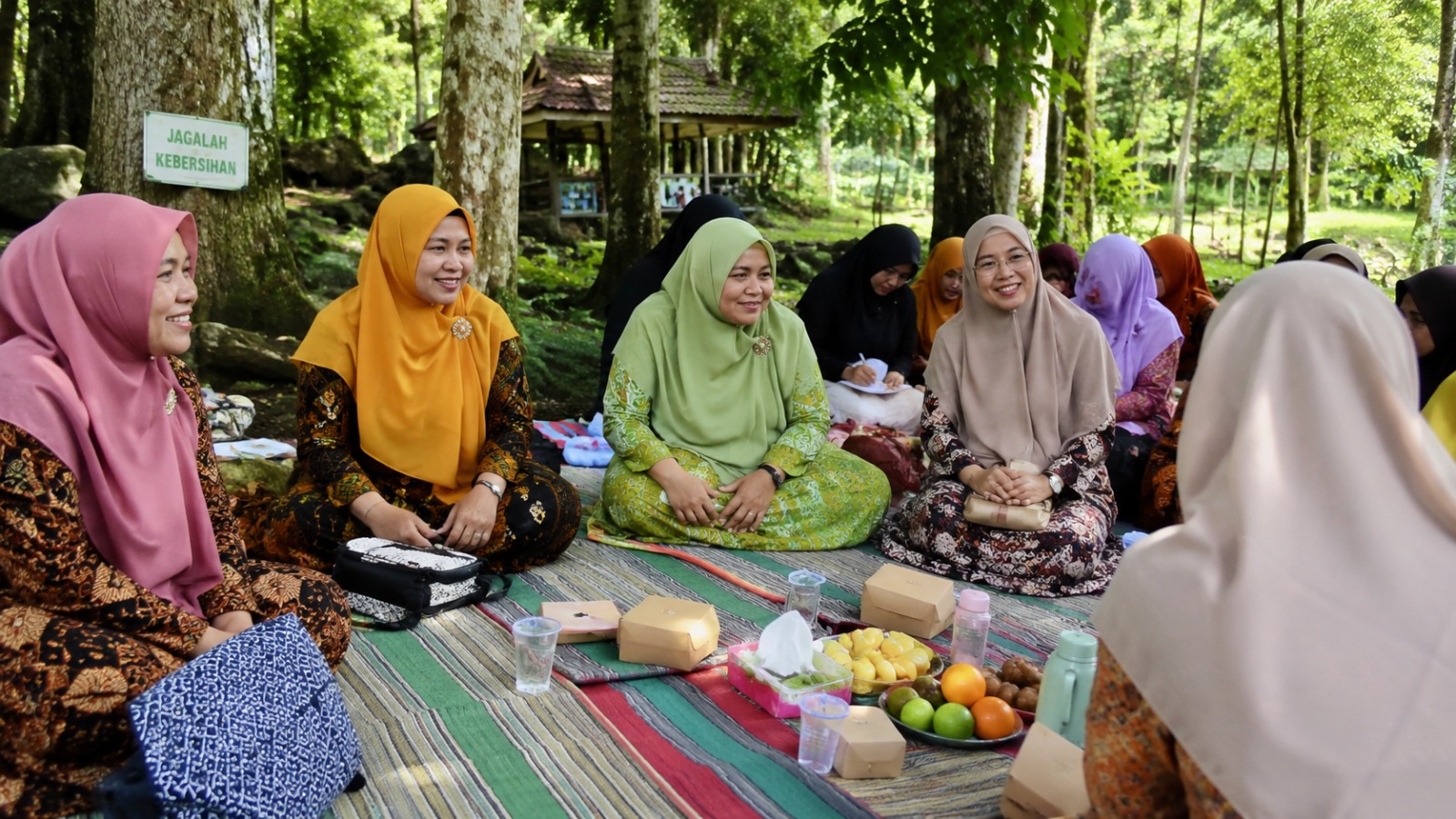 Rombongan ibu-ibu Majelis Taklim 'Aisyiyah duduk melingkar di atas tikar dalam ruang terbuka hijau di bawah rindangnya pepohonan, menyimak pengajian khusus dan menikmati kebersamaan dalam agenda wisata tadabur alam.