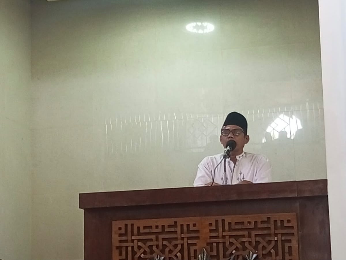 Ustaz Fathurrahman memakai peci hitam dan baju putih sedang menyampaikan khutbah Jumat tentang cara konsisten ibadah di balik mimbar kayu berukir di Masjid At Taqwa Semarang.