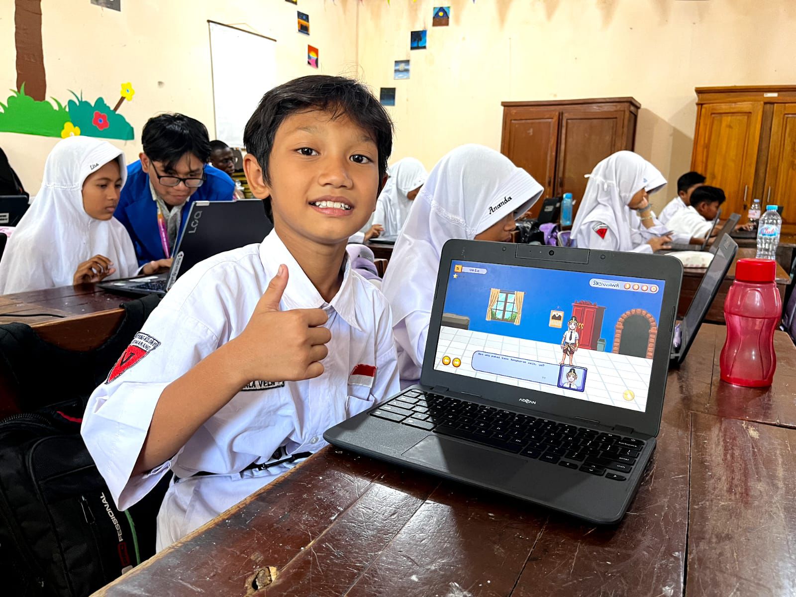 Siswa SD Negeri Kalibanteng Kulon 01 tersenyum sambil mengacungkan jempol di depan laptop yang menampilkan Game Sikapandawa sebagai media pendidikan karakter anak interaktif.