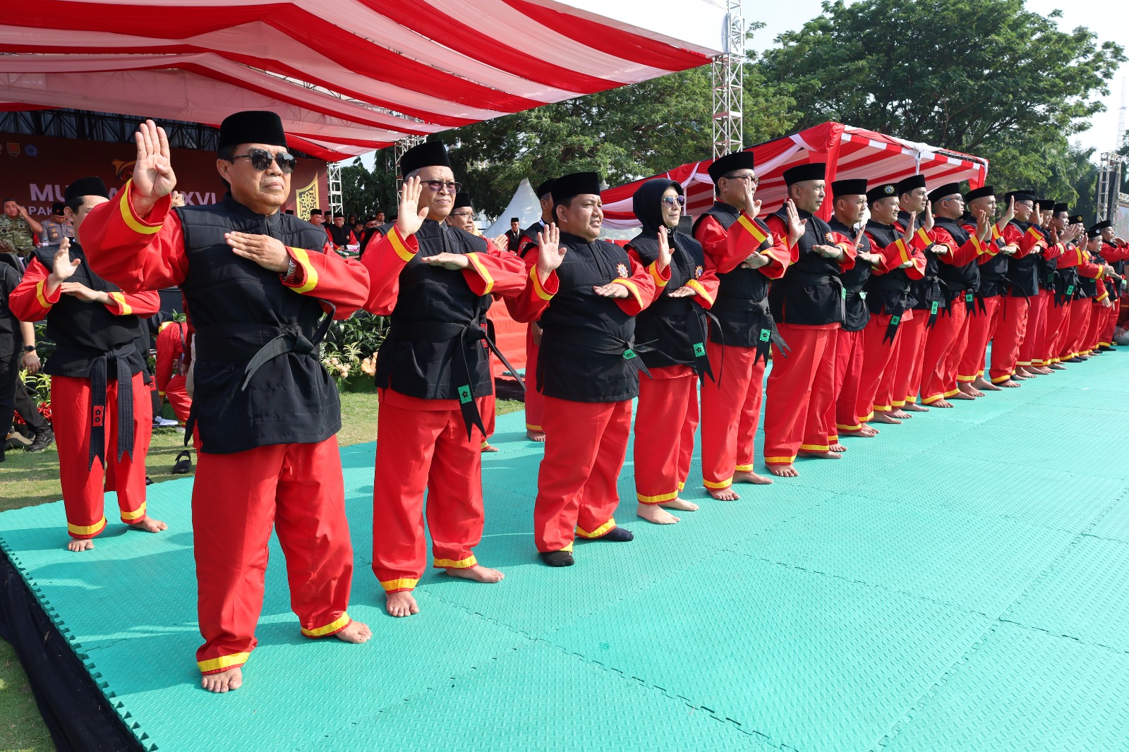 Deretan tokoh penerima gelar Pendekar Kehormatan Tapak Suci mengenakan seragam merah hitam beserta sabuk pendekar berdiri rapi memeragakan salam hormat Tapak Suci di atas matras hijau.