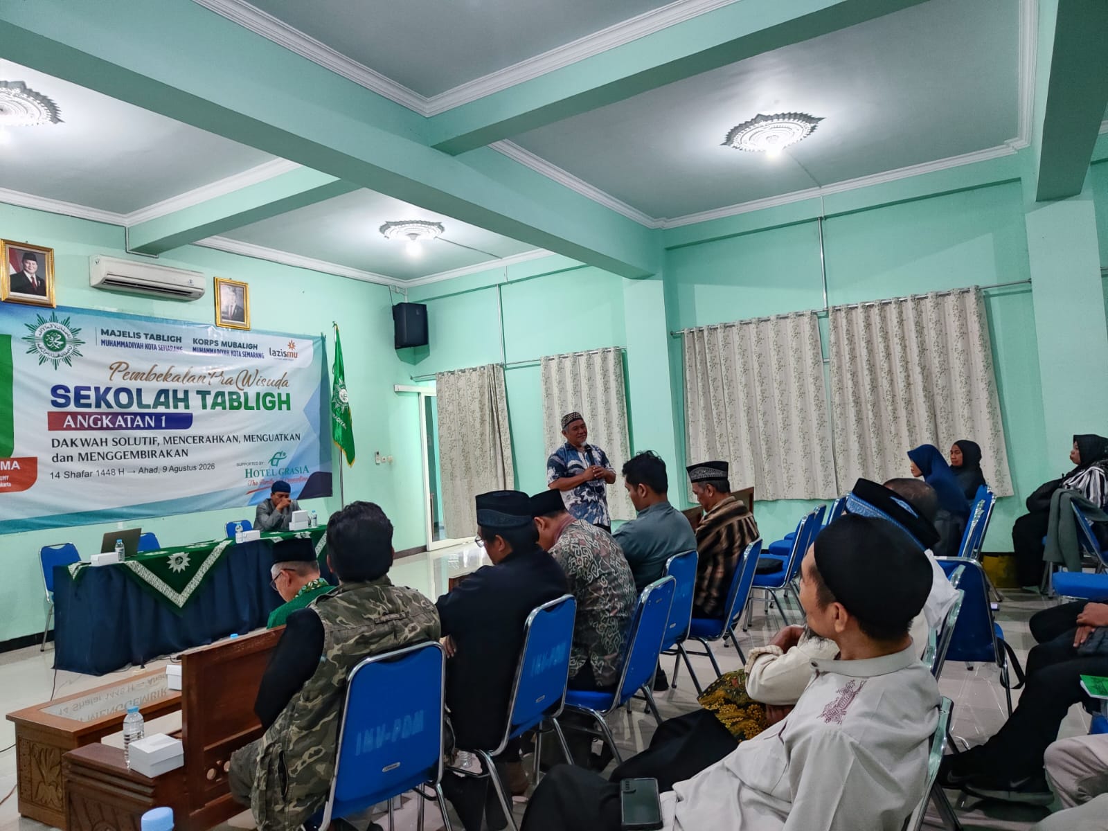 Penceramah Dr. Syakir Jamaluddin berdiri memaparkan materi di depan para peserta Sekolah Tabligh yang duduk rapi di ruangan bernuansa hijau.