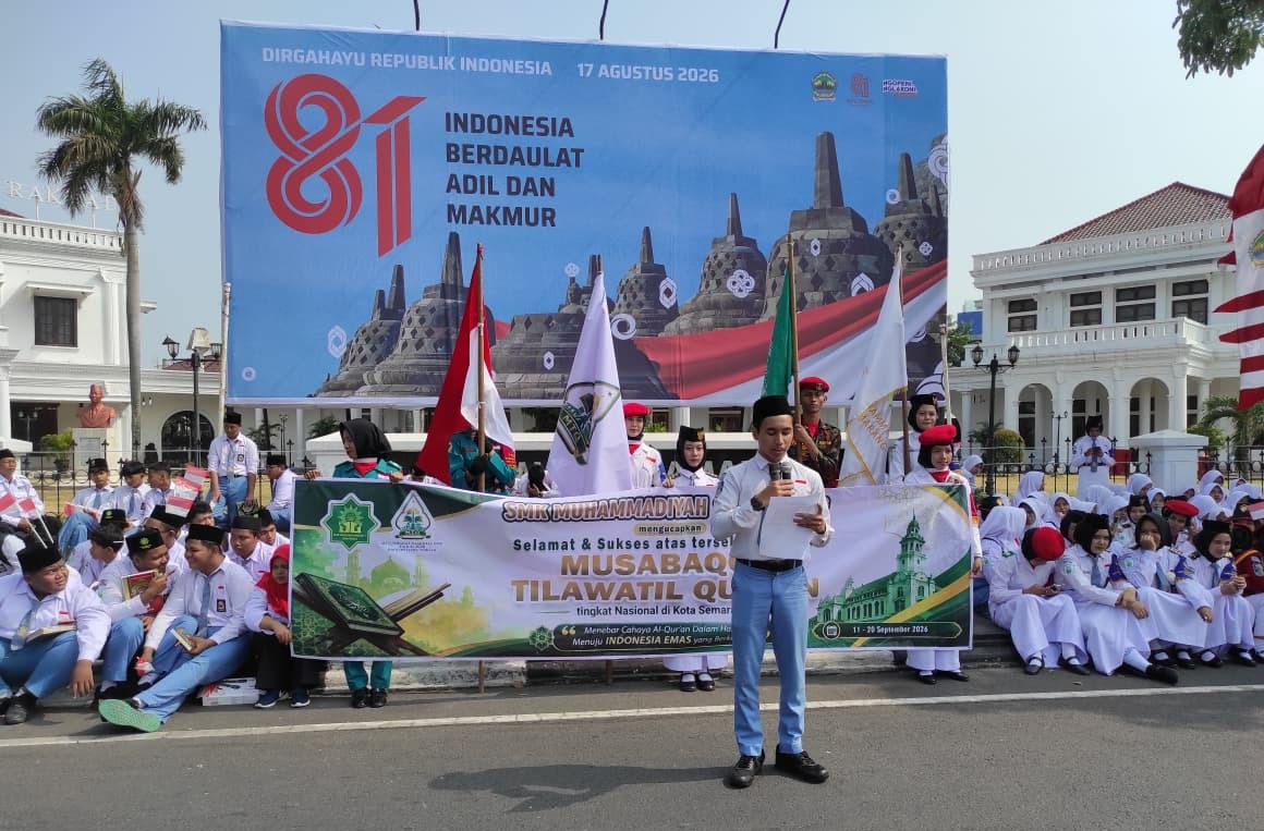 Seorang siswa berseragam abu-abu putih dan peci hitam membacakan naskah di depan spanduk ucapan MTQ Nasional dan baliho besar HUT RI ke-81 di Wisma Perdamaian Semarang, dikelilingi ratusan siswa dan pengibar bendera.
