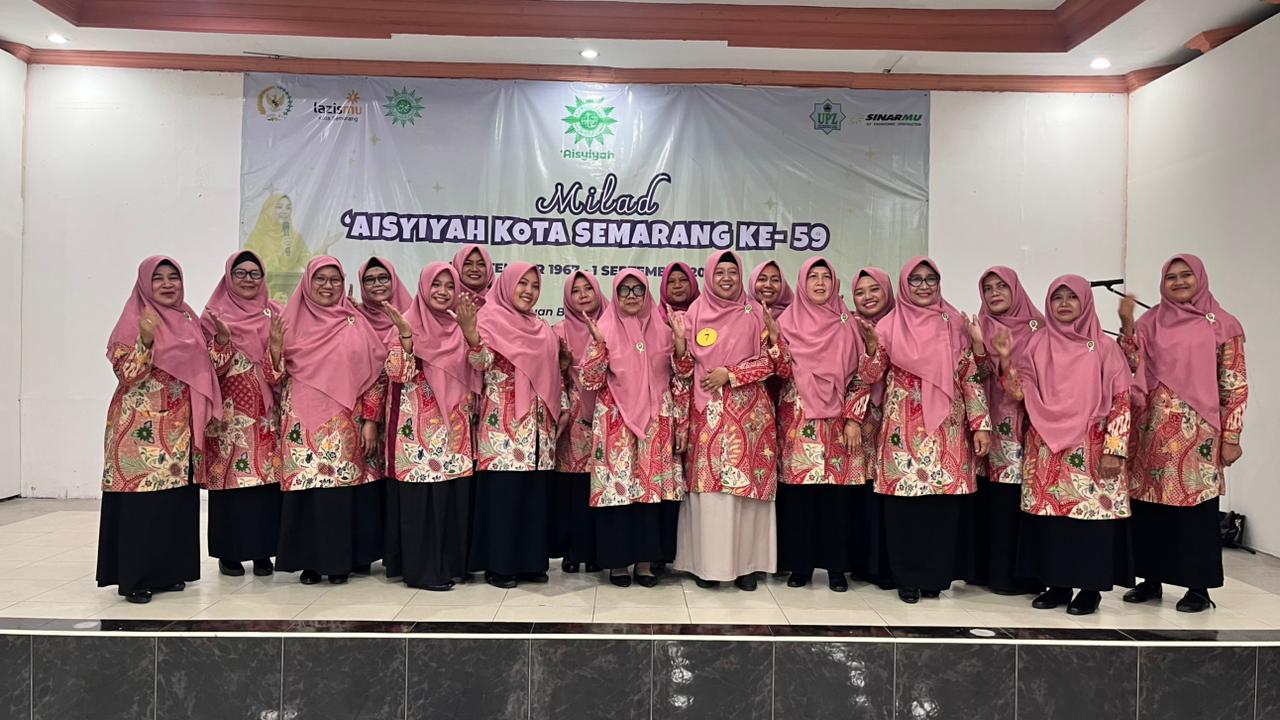 Anggota paduan suara PCA Ngaliyan mengenakan seragam batik merah bermotif dengan jilbab merah muda berdiri rapi di atas panggung aula RS Roemani Semarang dengan spanduk Milad 'Aisyiyah Kota Semarang Ke-59 di latar belakang.