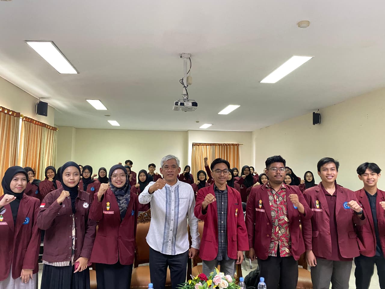 Sembilan pimpinan dan tamu undangan termasuk Dr. M. Fatkhul Mubin dan pimpinan IMM mengenakan jas merah marun berdiri dengan pose mengepalkan tangan di depan puluhan peserta DAD PK IMM Ar Razy Unimus di dalam ruang aula.