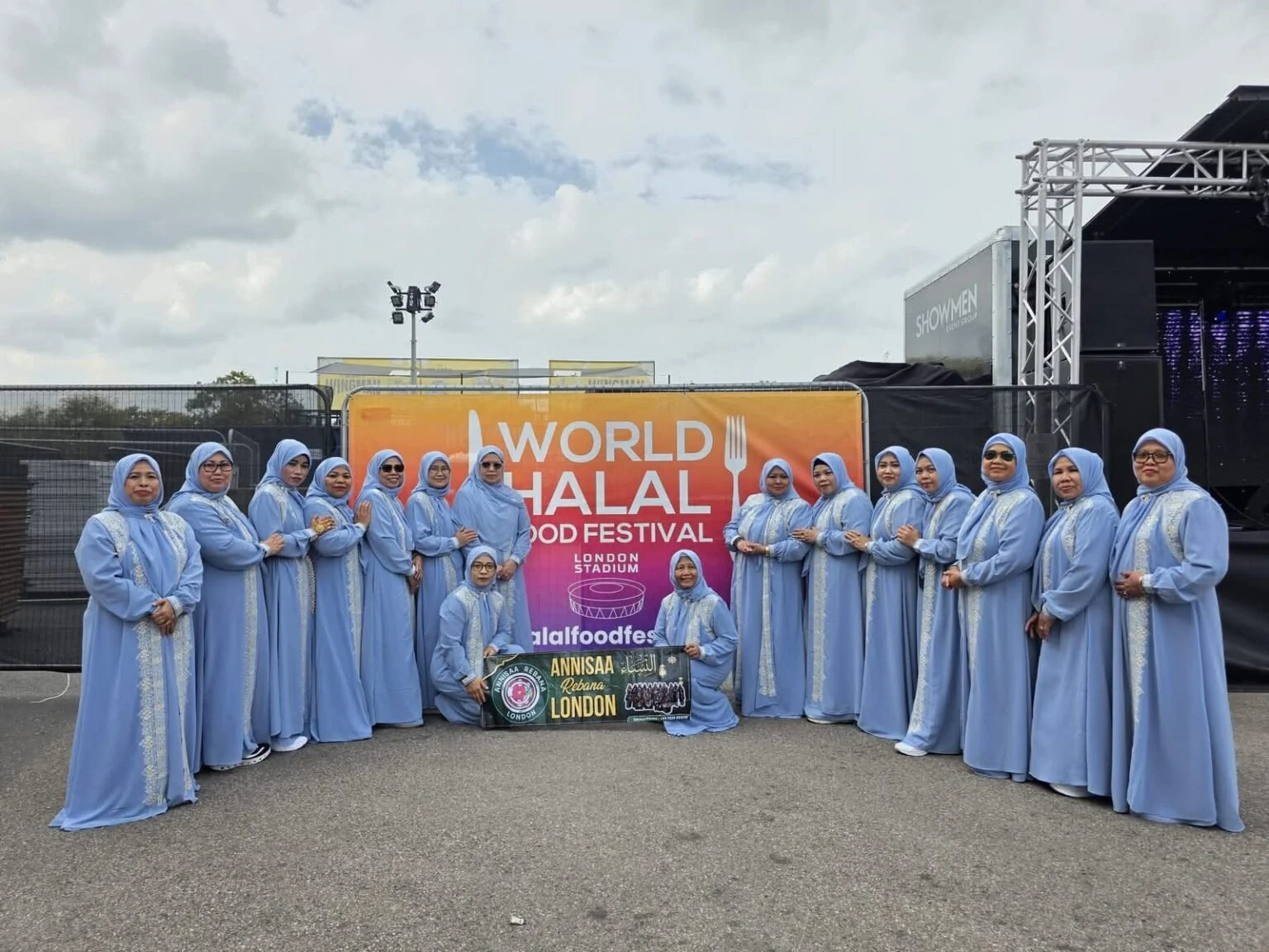 Kelompok qasidah diaspora Annisa Rebana London berpose mengenakan gamis biru muda di depan latar World Halal Food Festival di London Stadium.